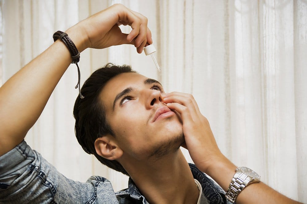 Handsome young man dropping medicine in his eye with eye-dropper